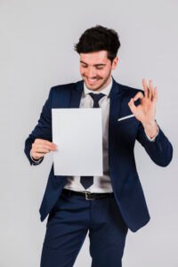 handsome young businessman holding white paper hand showing ok sign against grey backdrop